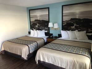 A hotel room with two beds, each with a patterned bedspread, a nightstand with a lamp, and a wall-mounted light fixture. - Northgate Motel (El Cajon)