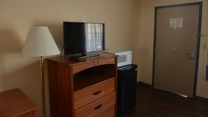 Une pièce comprenant une commode en bois, un téléviseur posé dessus, une lampe blanche, un four à micro-ondes et une poubelle.