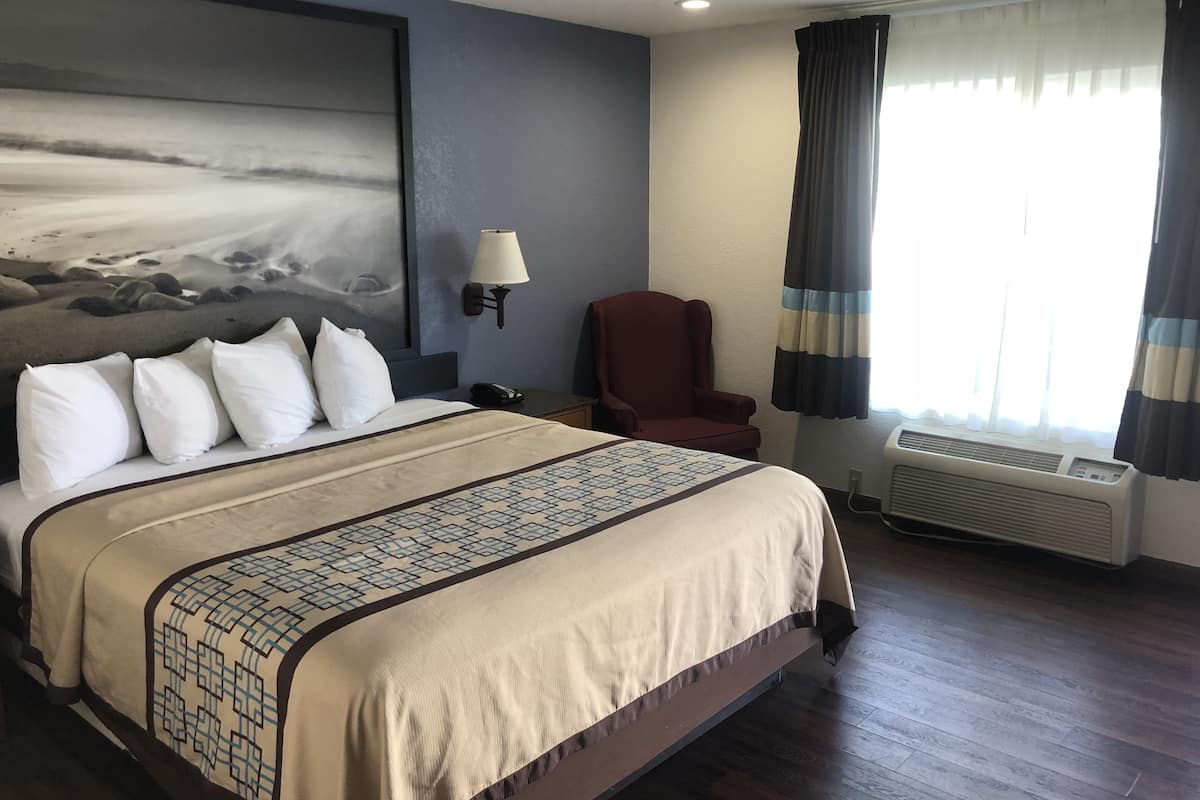 A hotel room with a large bed, a chair, a wall-mounted lamp, and a window with curtains.