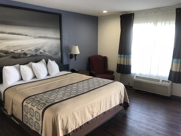 A hotel room with a large bed, a chair, a wall-mounted lamp, and a window with curtains. - Northgate Motel (El Cajon)