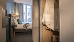 Habitación de hotel con cama, mesita de noche con lámpara, ventana con cortinas y zona de ducha con cortina de leopardo.