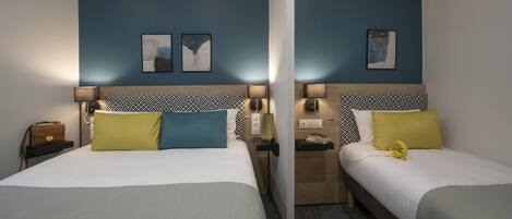 Two twin beds with matching headboards, a nightstand with a lamp, a small table with a lamp, and a wall-mounted artwork.