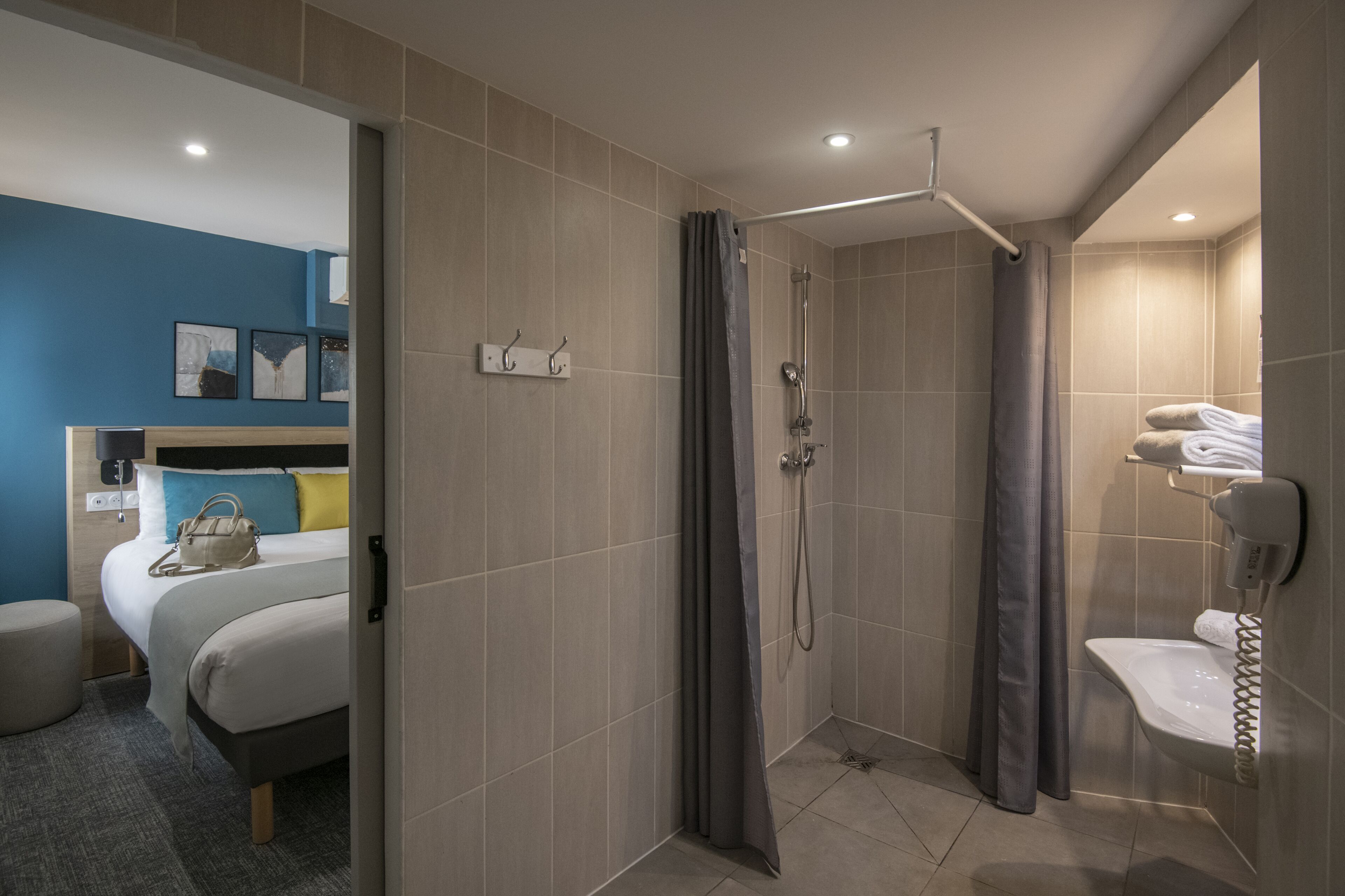 Una habitación de hotel moderna con ducha, una cama con cabecera, una mesita de noche y un perchero para toallas en la pared.