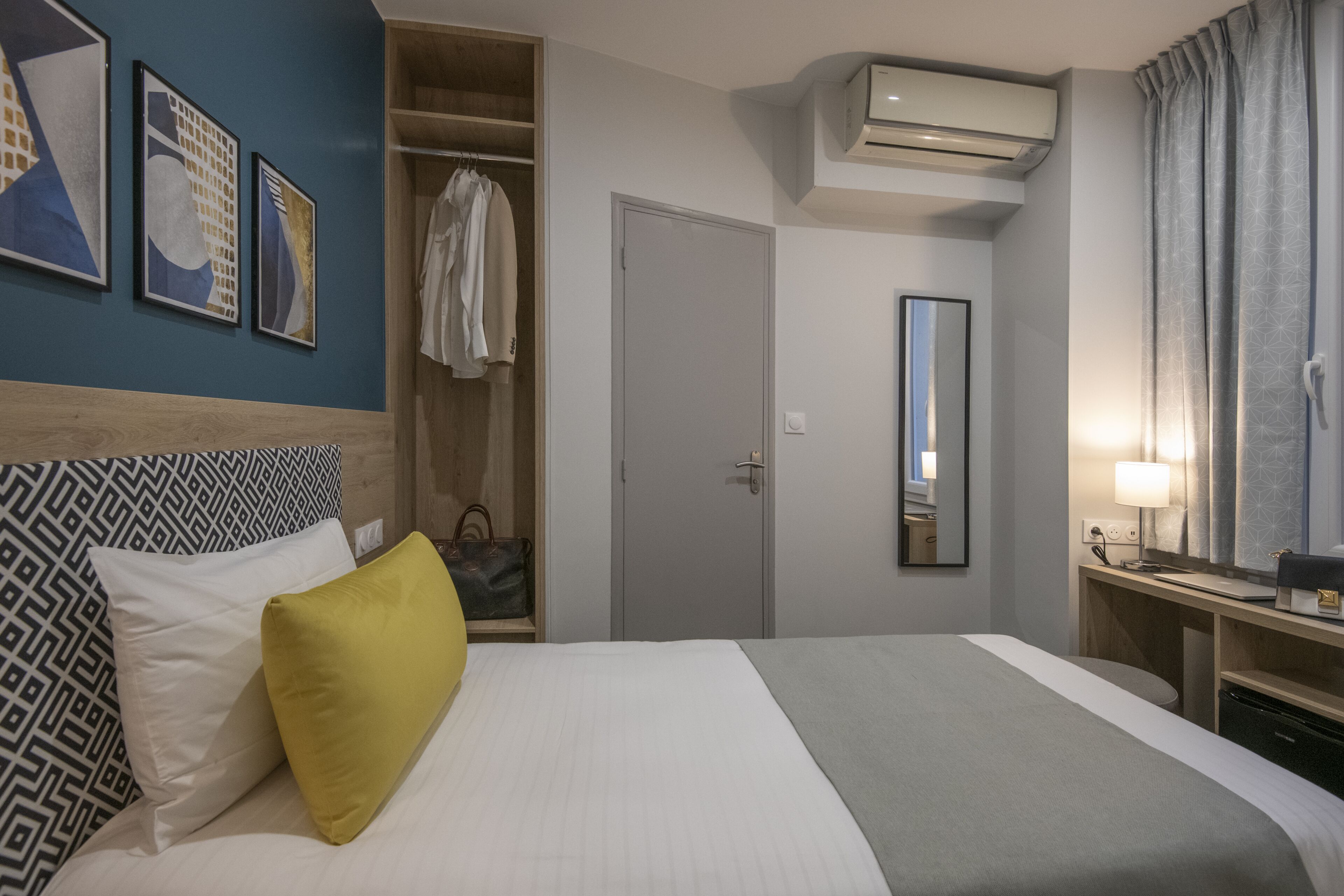 A hotel room with a bed, a wardrobe, a mirror, and an air conditioning unit.