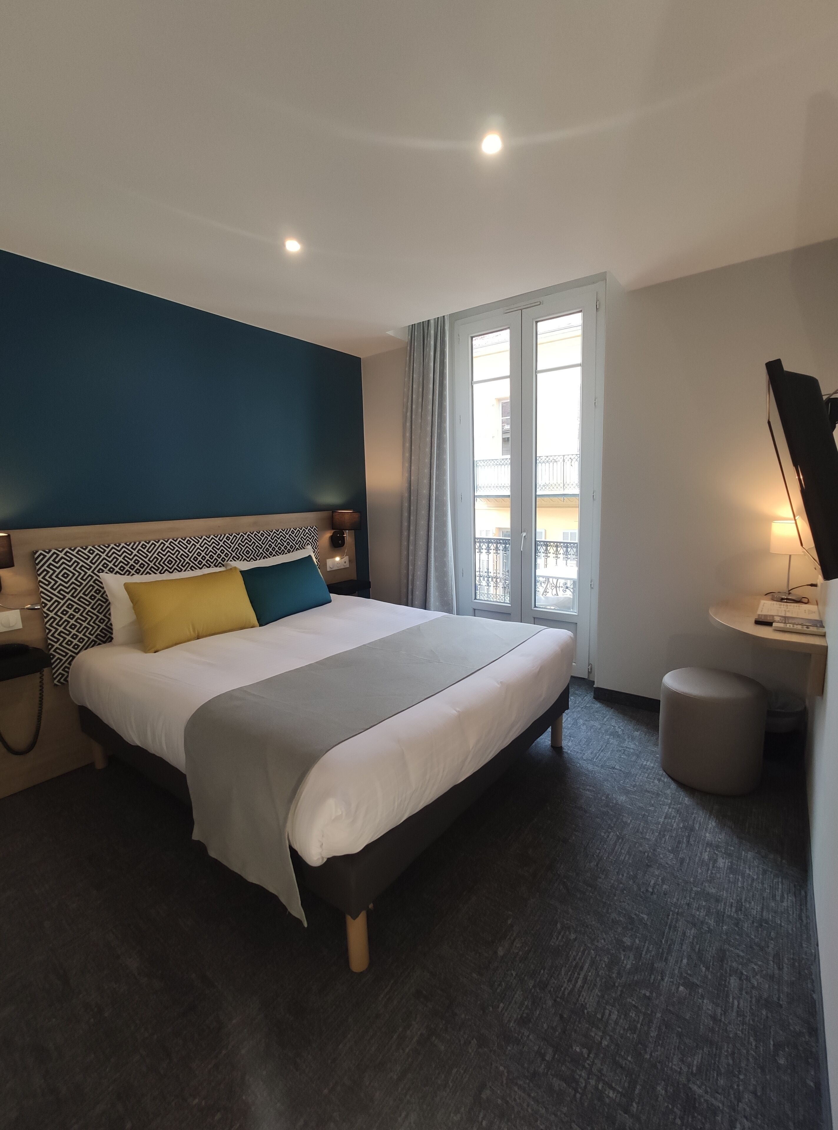 Habitación de hotel moderna con una cama grande, un escritorio y vistas al balcón exterior.