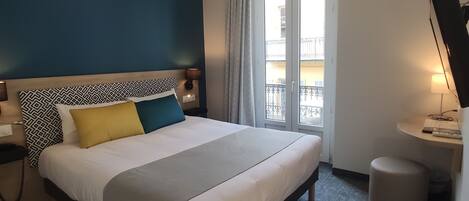 Habitación de hotel moderna con una cama grande, un escritorio y vistas al balcón exterior.
