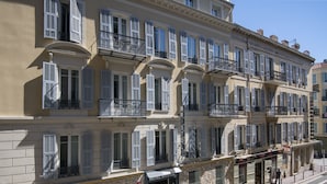 Un hotel de varios pisos con balcones, fachada de piedra y cielo azul despejado.