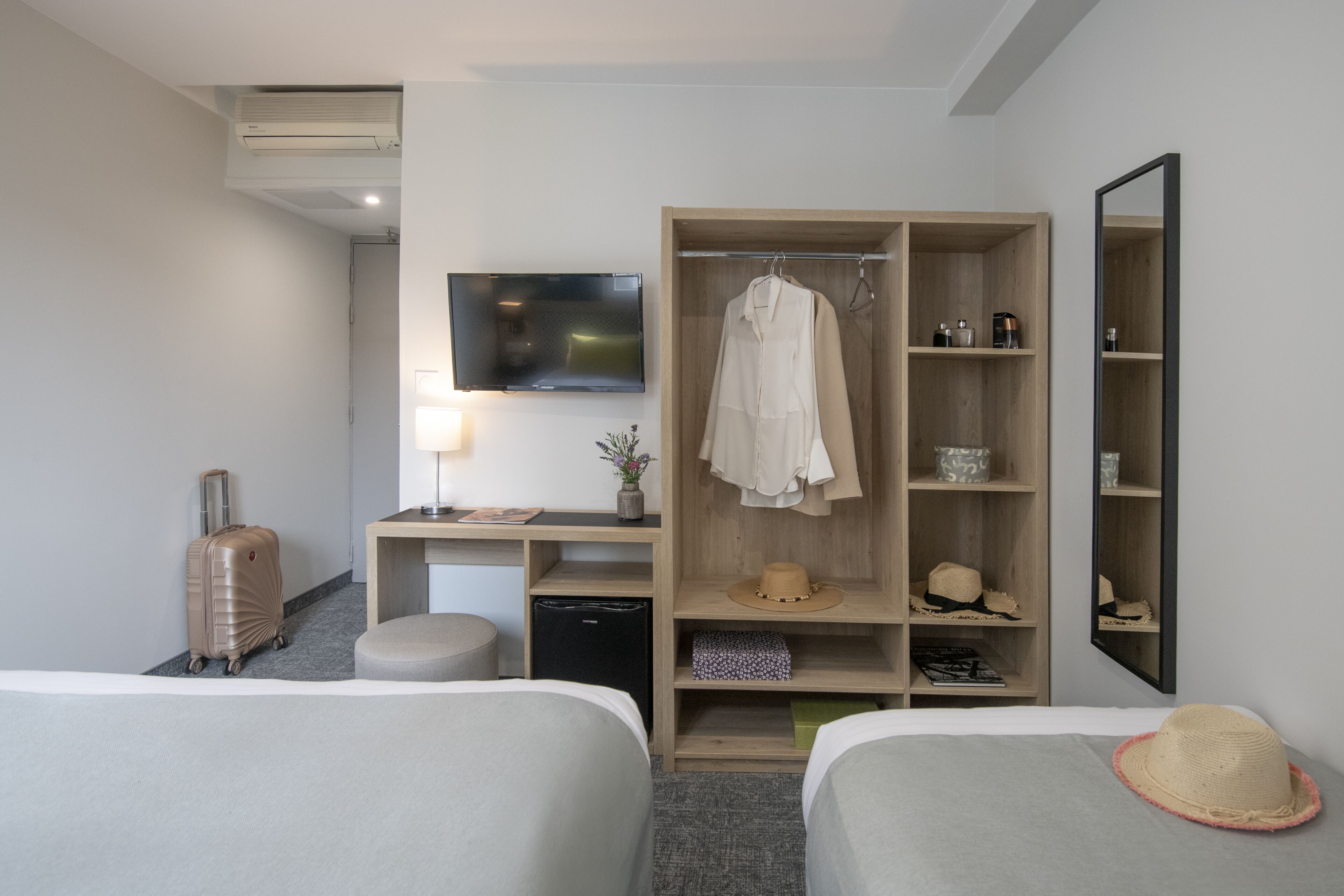 Une chambre d’hôtel avec deux lits, un bureau avec une télévision, une armoire et un miroir.