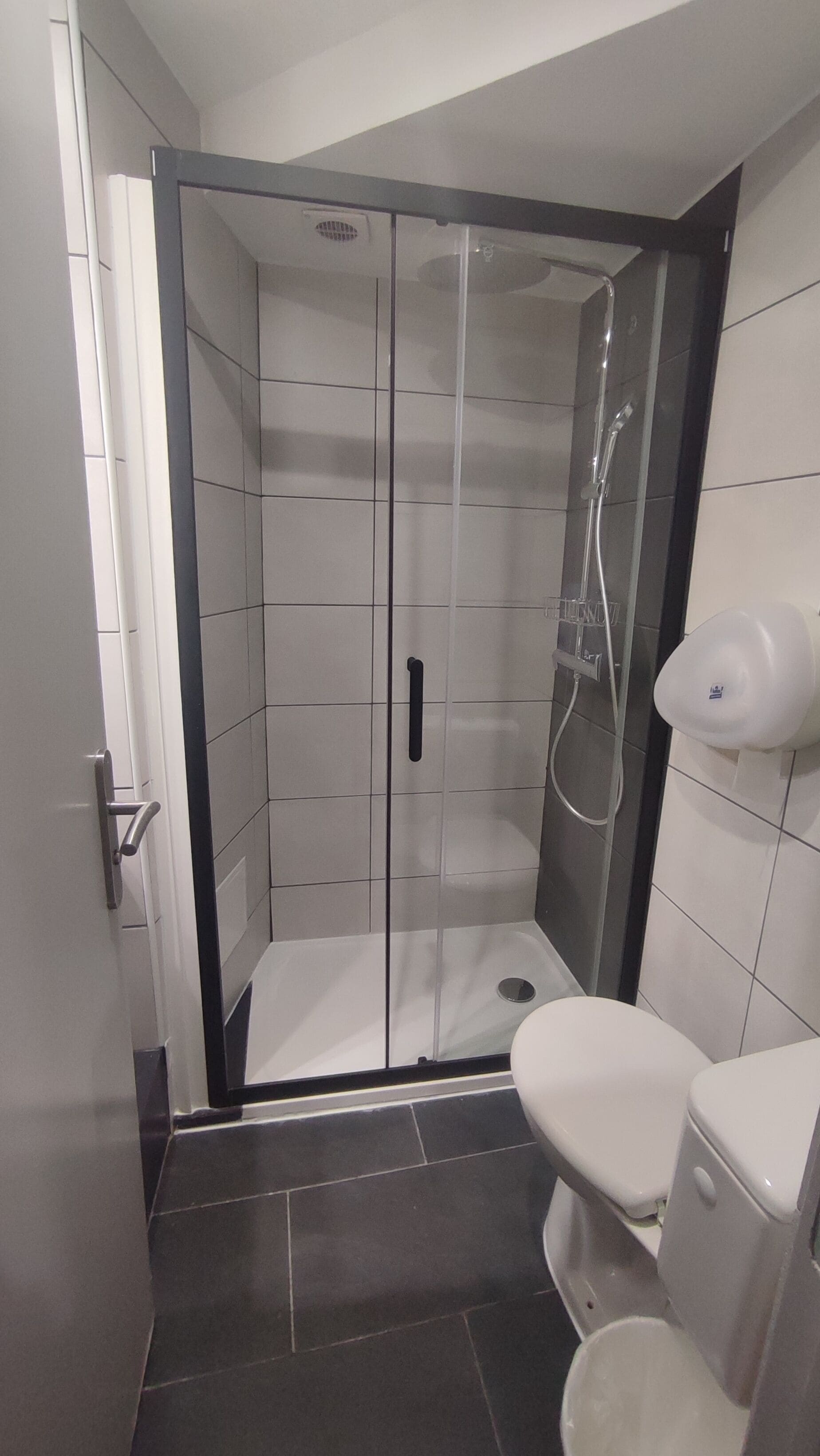 A modern bathroom with a glass-enclosed shower, a toilet, and a hand dryer.