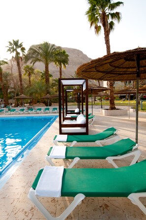 A poolside area with lounge chairs and umbrellas, palm trees, and a mountain in the background. - Leonardo Inn Hotel Dead Sea (Tamar)
