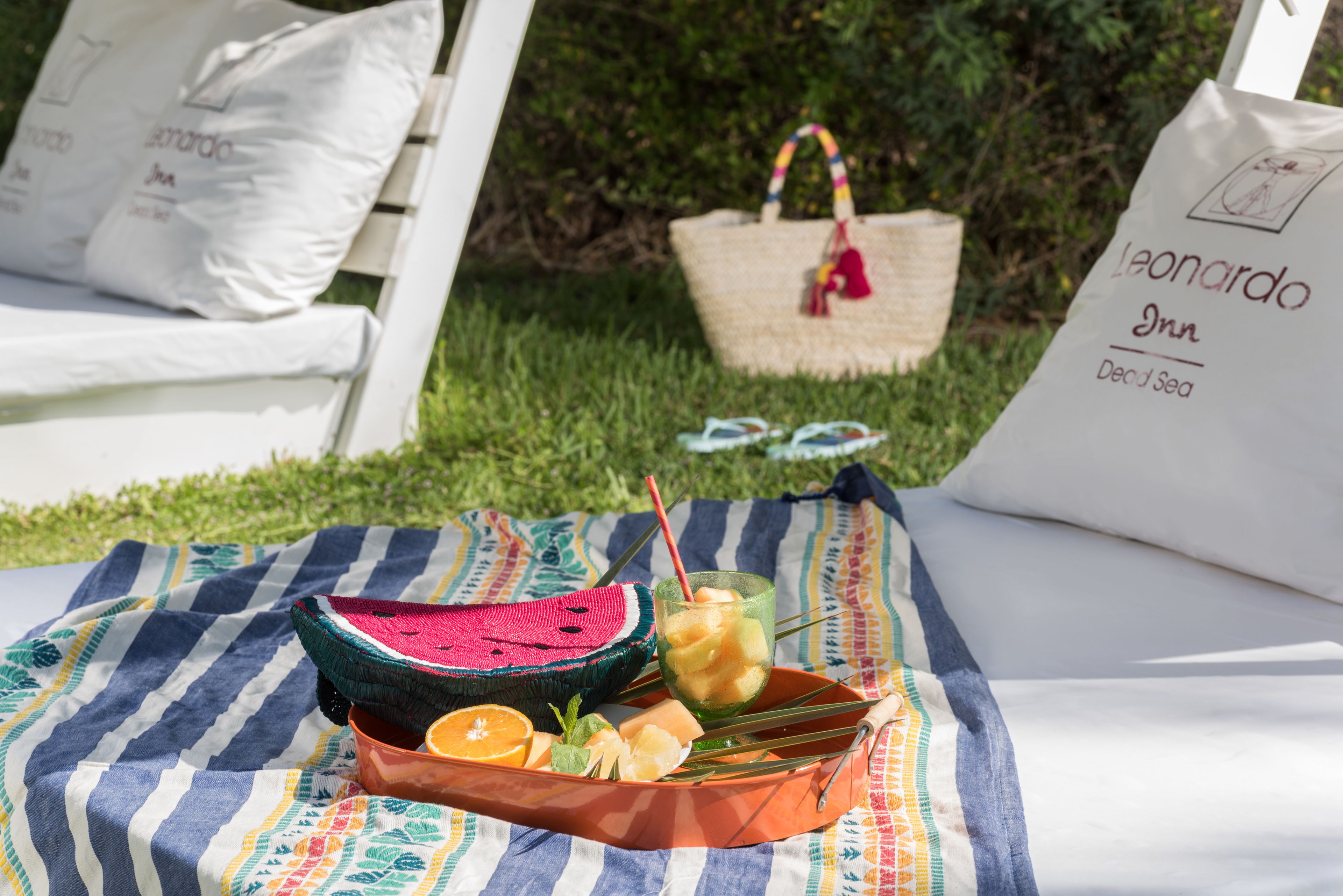 A picnic setup with a watermelon, orange slices, and a drink on a striped blanket.
