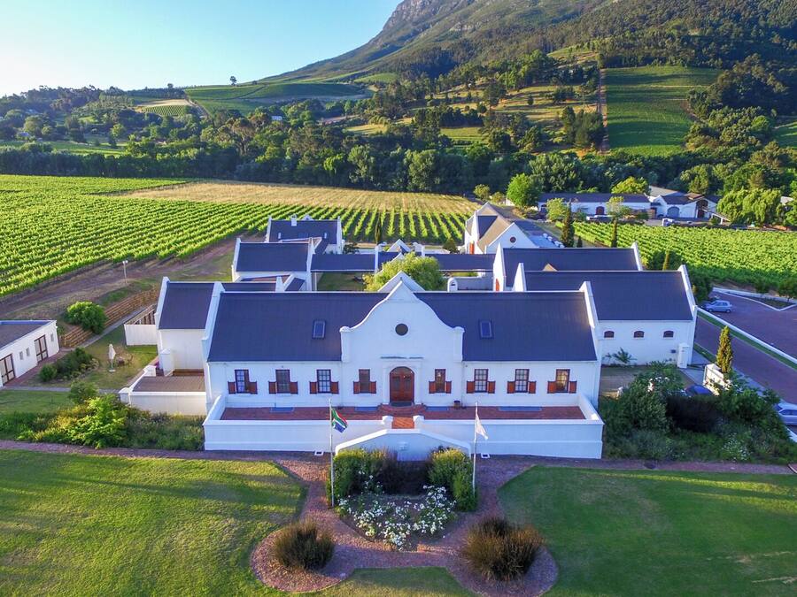 A large estate with a central building surrounded by vineyards, a driveway, and a well-maintained lawn.