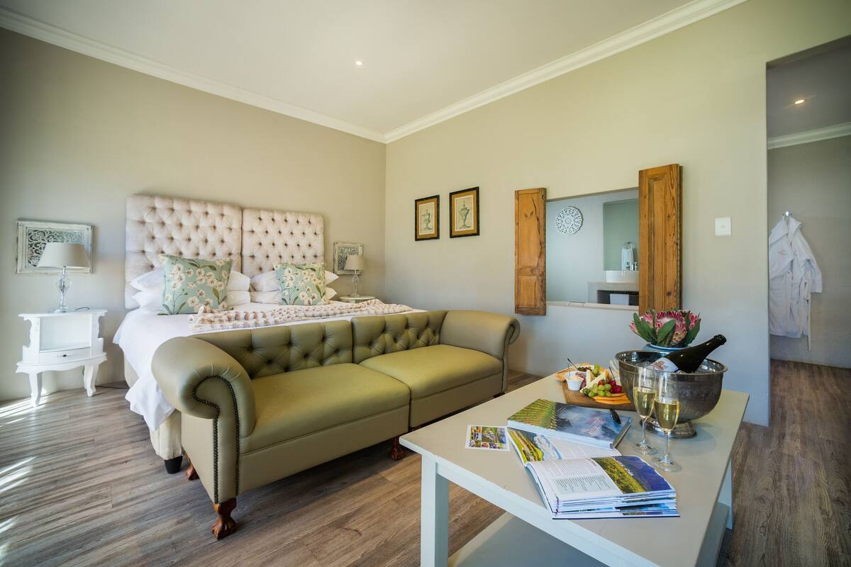 Une chambre à coucher comprenant un lit, un canapé vert, une table de chevet, une commode, un miroir et une petite salle de bain.