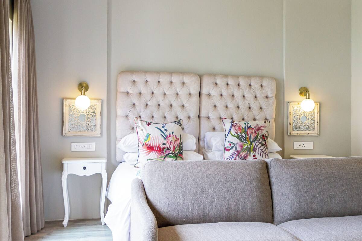 Une chambre à coucher avec une tête de lit capitonnée, deux tables de chevet, un canapé et des appliques murales décoratives.