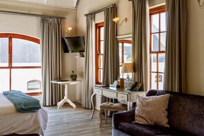 Une chambre d’hôtel équipée d’un lit, d’un bureau, d’une chaise, d’un canapé, d’une télévision et de grandes fenêtres.