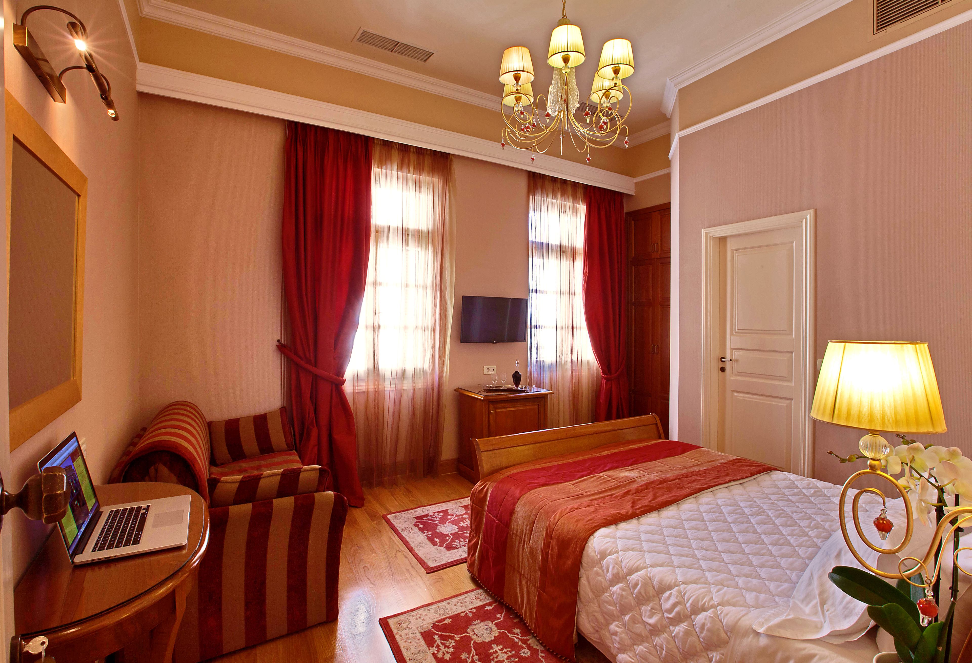 Een hotelkamer met een bed, een bureau met een laptop, een televisie en een lamp.