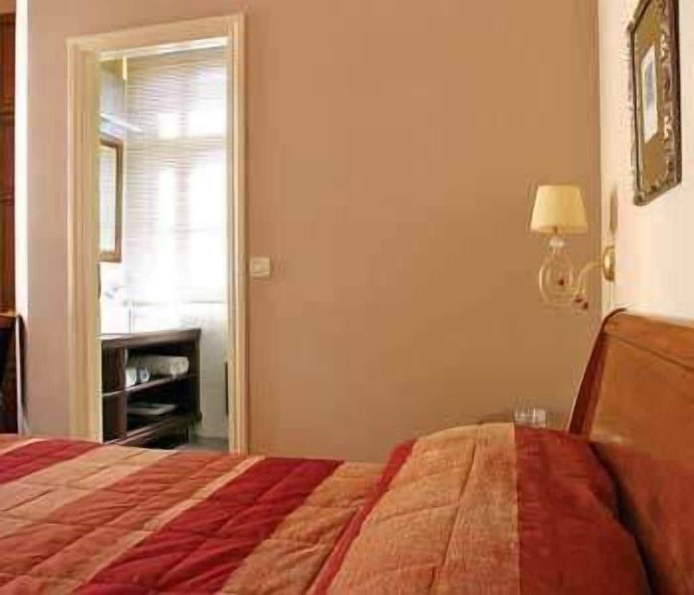 A bedroom with a bed, a nightstand, a lamp, and a door leading to another room.