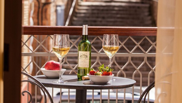 A balcony with a table set for two, featuring a bottle of wine, two glasses, a bowl of strawberries, and a plate of food. - Aetoma Hotel (Nafplio)