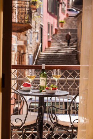 Un balcón con una mesa dispuesta para dos personas, que incluye una botella de vino, dos copas, un bol de fresas y un plato de comida.