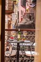Un balcón con una mesa dispuesta para dos personas, que incluye una botella de vino, dos copas, un bol de fresas y un plato de comida.