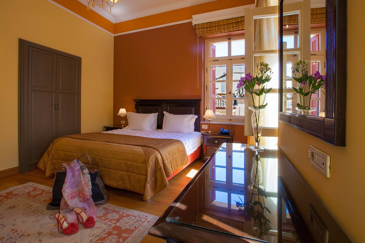 A well-lit bedroom with a large bed, bedside tables, a dresser, and a mirror.