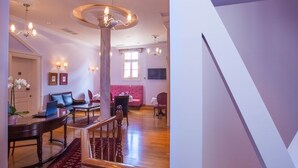 A spacious living area with a wooden staircase, a pink sofa, and a dining table with chairs. - Aetoma Hotel (Nafplio)