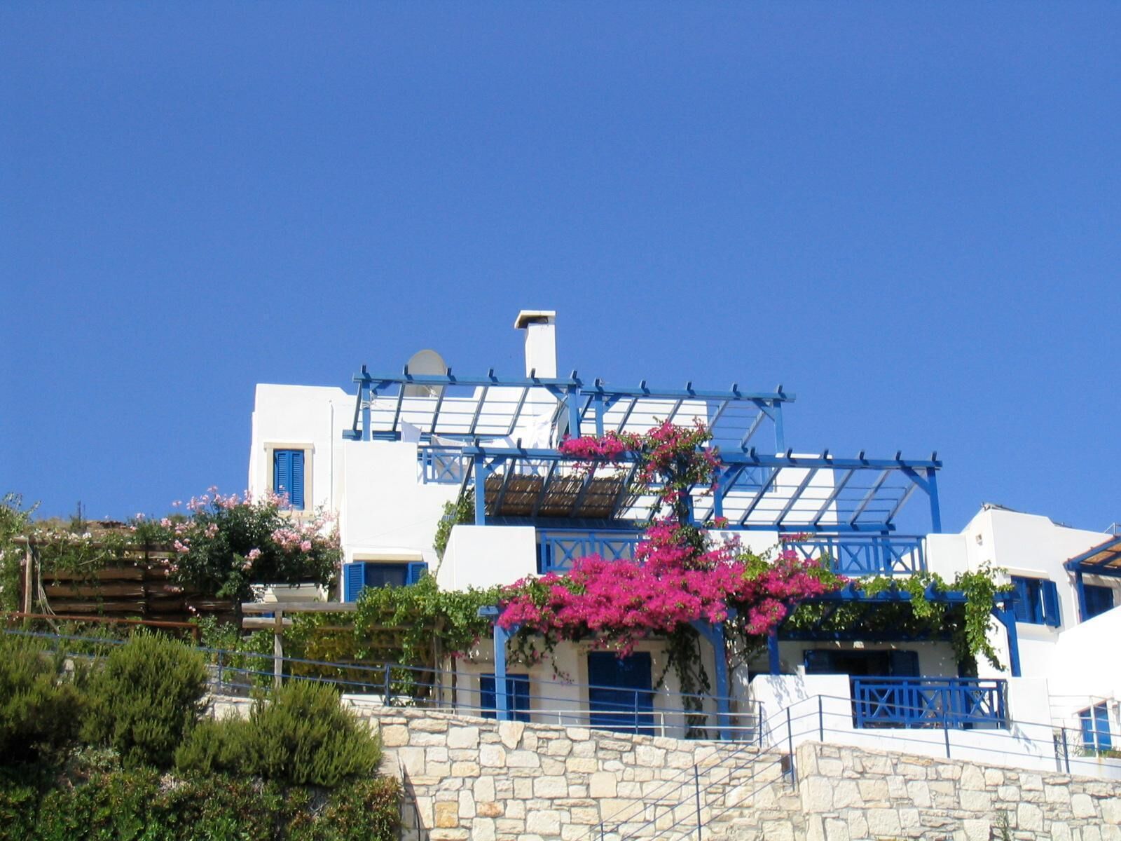 A white building with blue accents, a stone staircase, and pink bougainvillea.