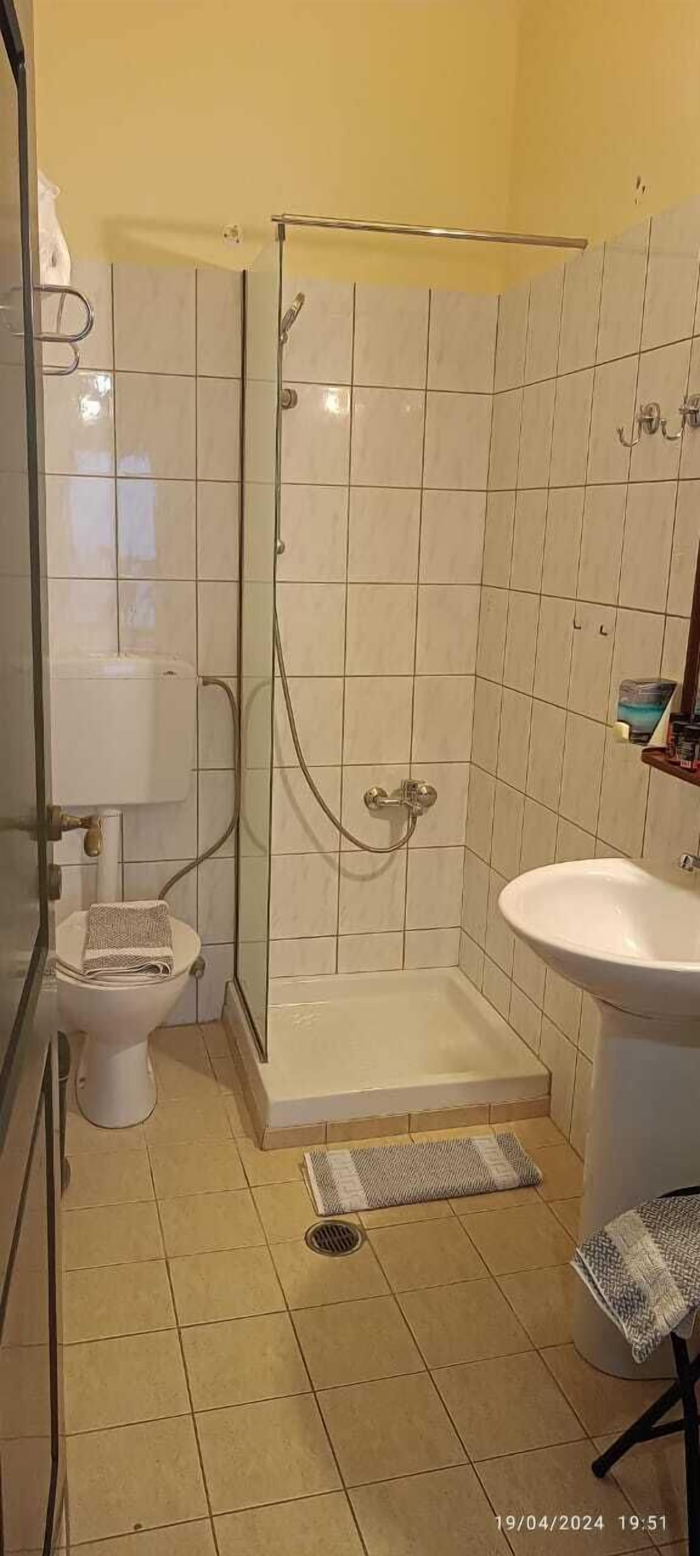 Un baño con ducha de mampara de vidrio, inodoro y lavamanos.