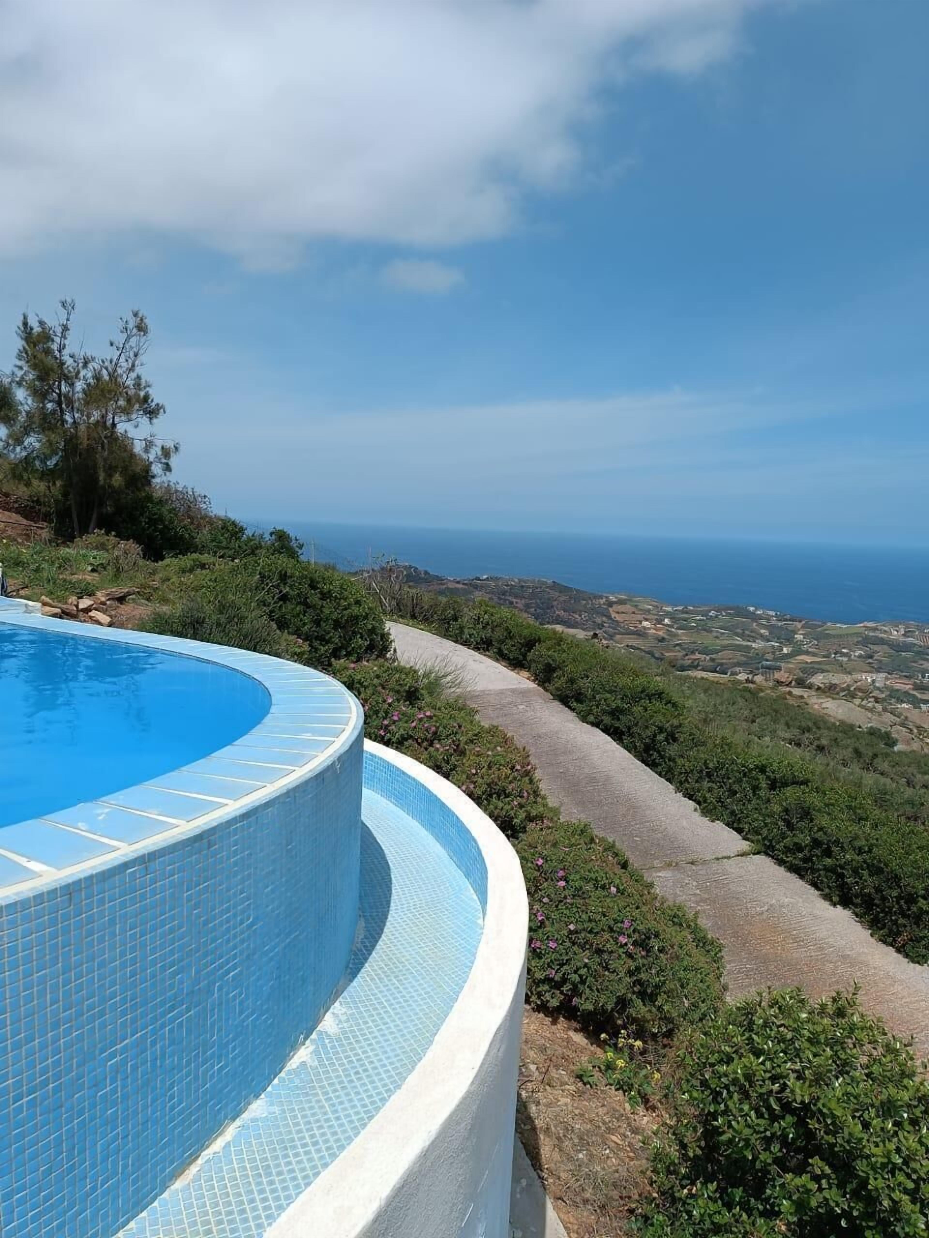 A curved swimming pool with a clear view of the ocean and distant landscape.