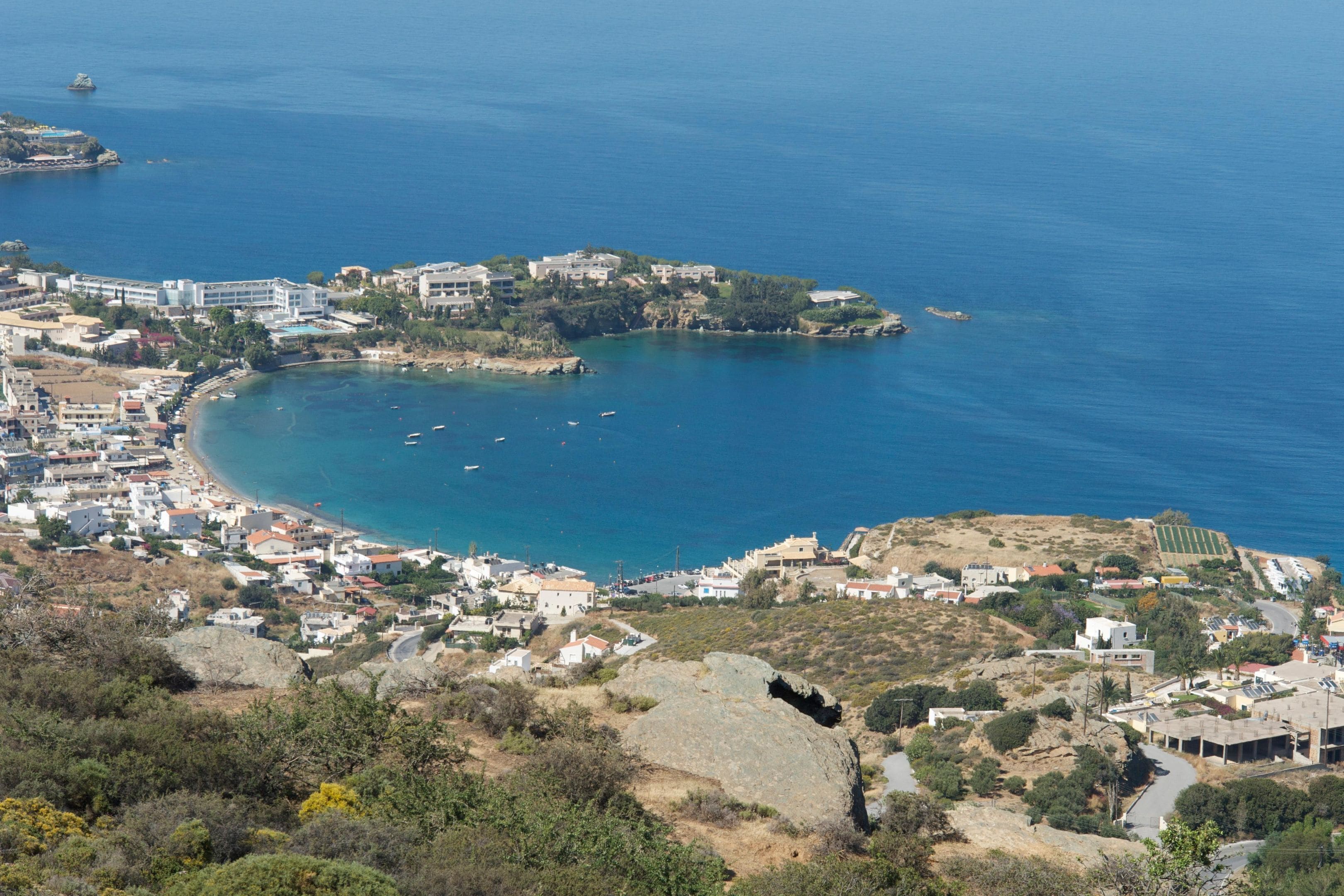 Un pueblo costero con edificios a lo largo de la orilla, una pequeña isla con construcciones y barcos en el agua.