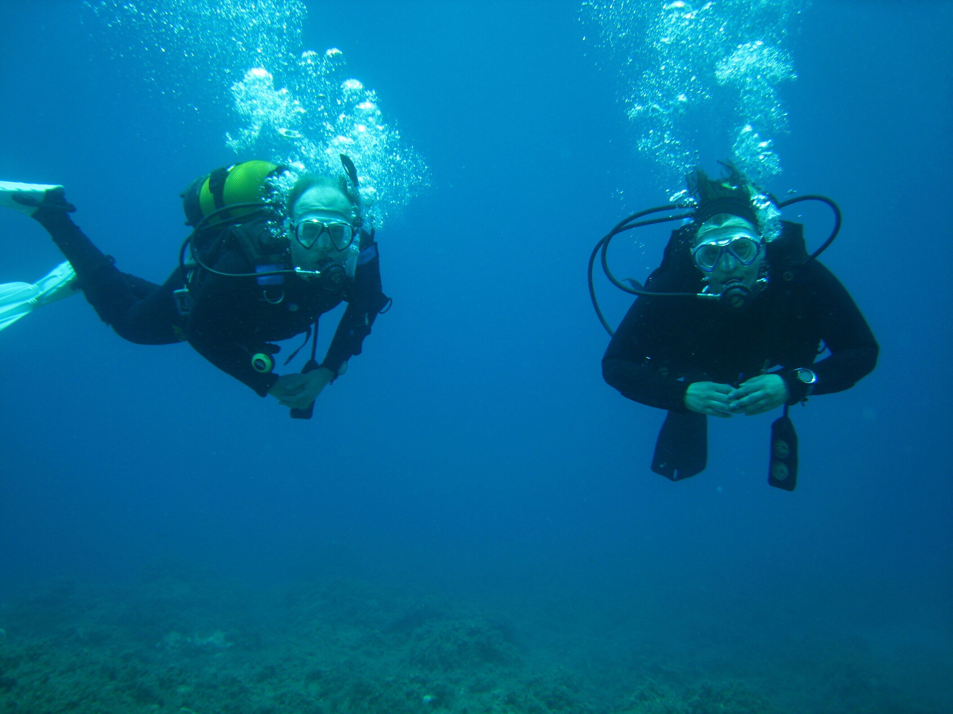 Two scuba divers underwater with bubbles around them.