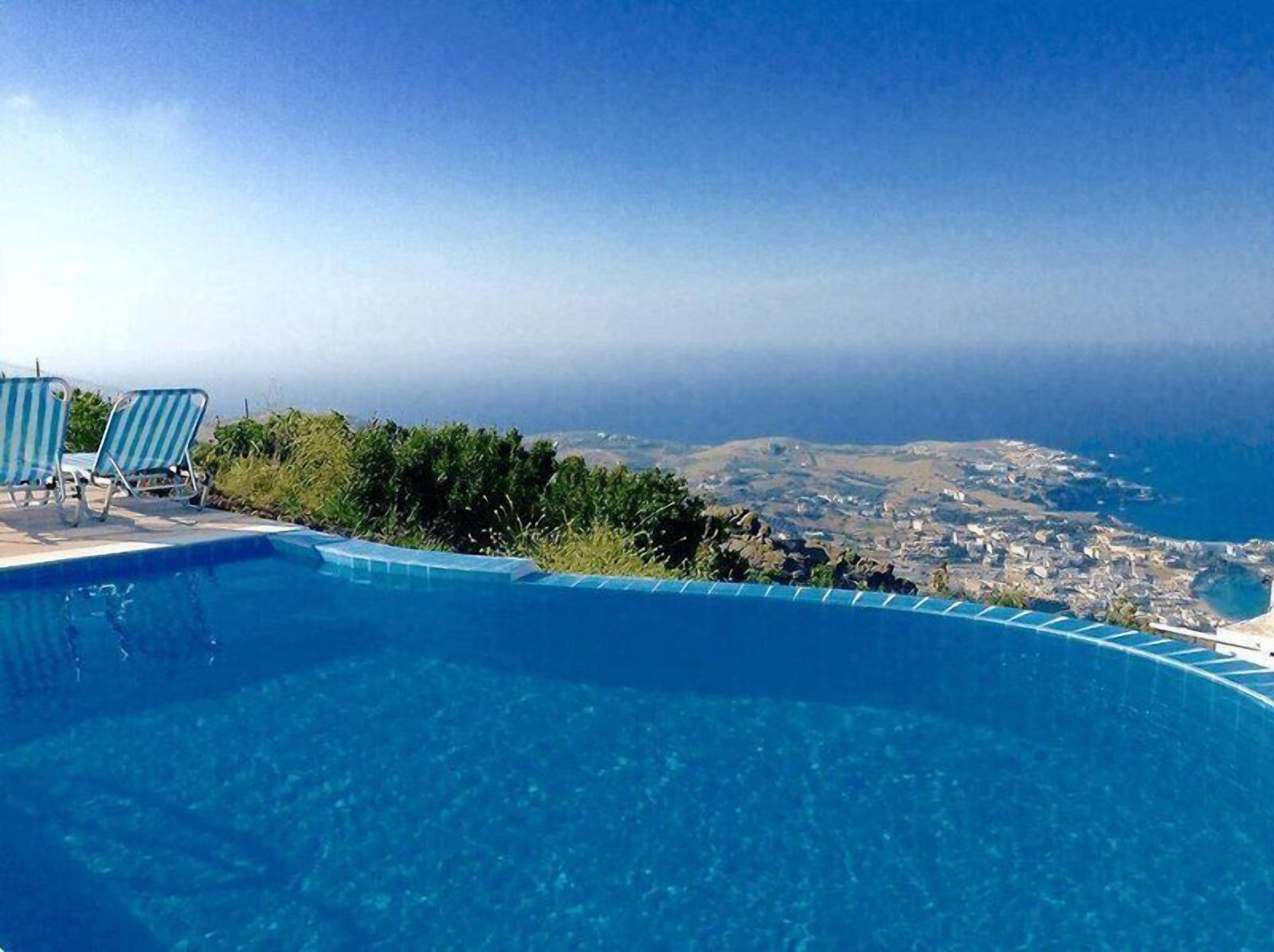 Une piscine avec deux chaises longues, offrant une vue sur un paysage côtier.