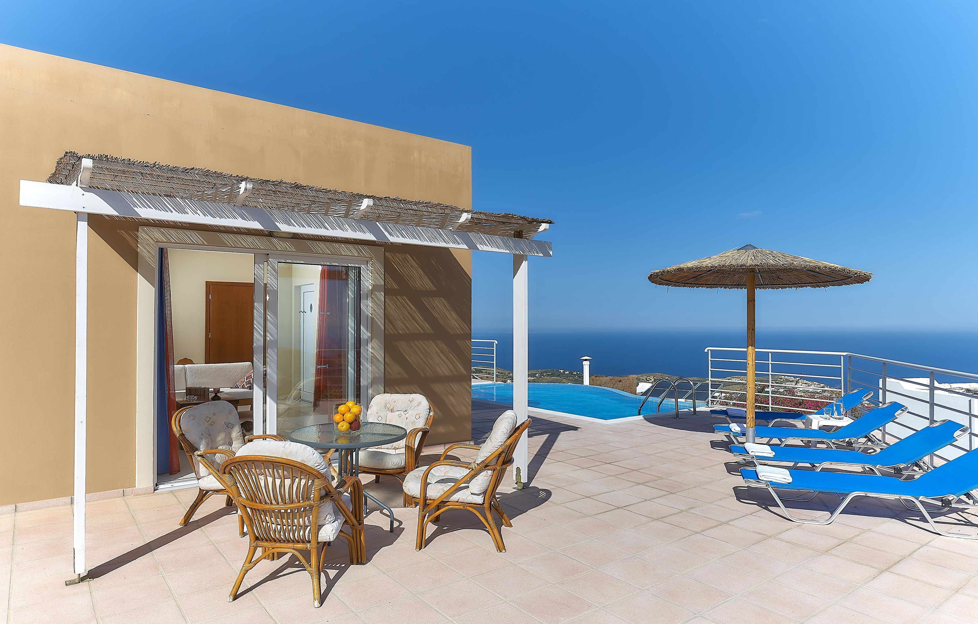 Une terrasse avec des fauteuils en osier, une table et une vue sur la mer.