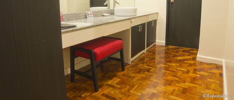 Un baño con piso de madera, una banca, un lavamanos y armarios.