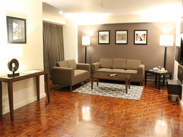 A living room with a sofa, coffee table, and a TV. There are three framed pictures on the wall and a lamp on each side of the sofa.