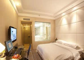 A hotel room with a bed, a desk with a computer, a television, and a window with a view of a building. - Jin Jiang Sun Hotel (Lanzhou)
