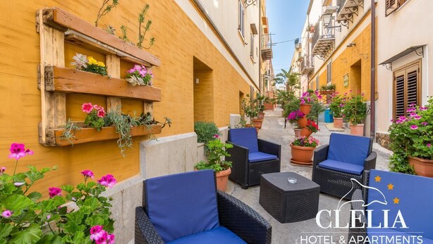 Una calle estrecha con mesas al aire libre, plantas en macetas y un estante de madera con flores.