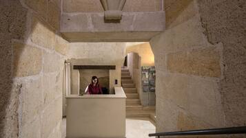 Interior con paredes de piedra, una recepción, una escalera y una máquina expendedora.