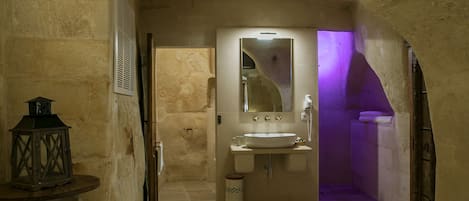 Une petite salle de bain aux murs de pierre, avec un lavabo blanc, un miroir et un éclairage violet.