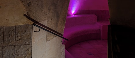 Una escalera con barandilla que conduce a una habitación con un rincón iluminado en rosa.