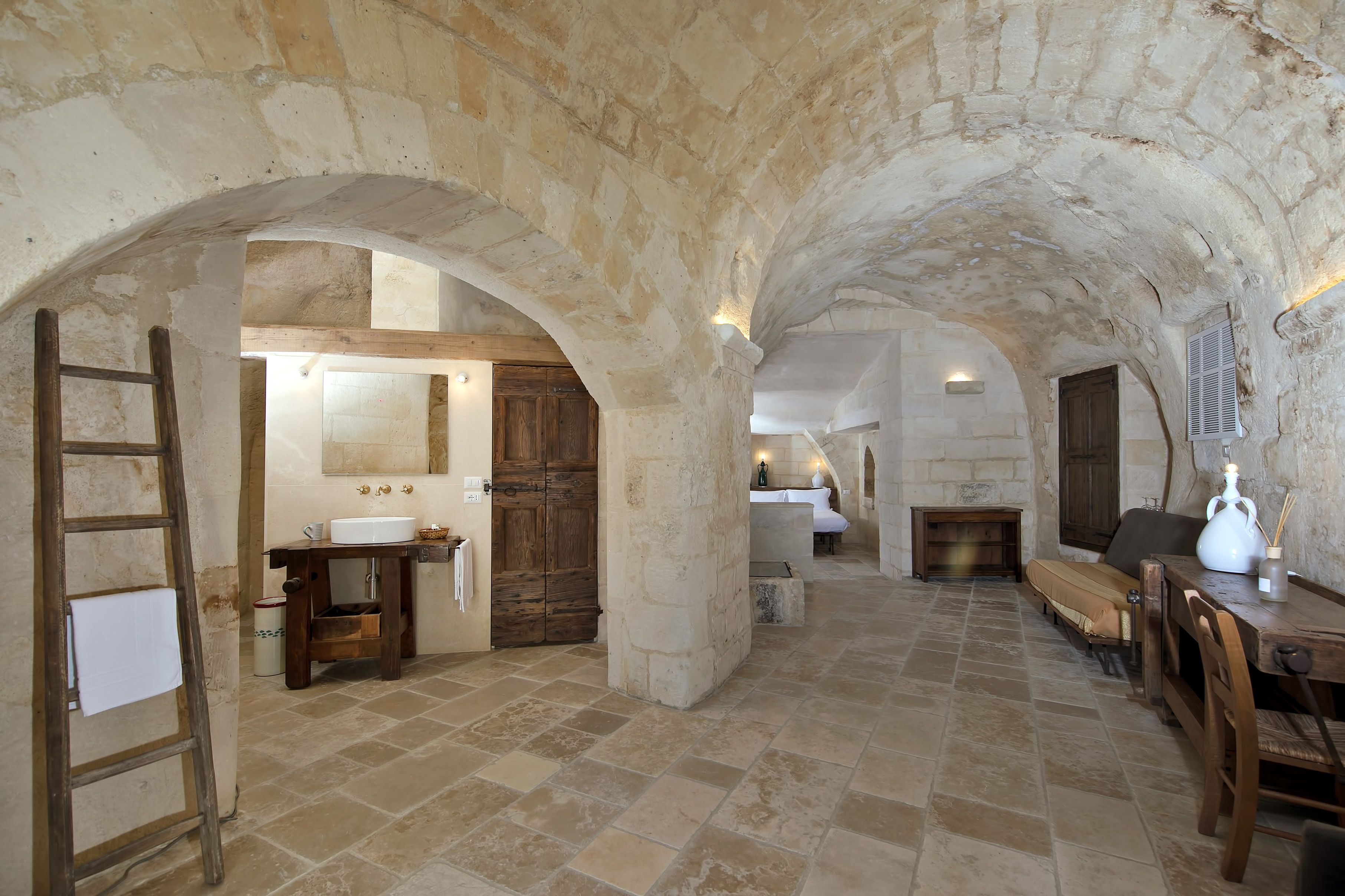 Un intérieur rustique avec des arches en pierre, une échelle en bois, un évier et un banc.