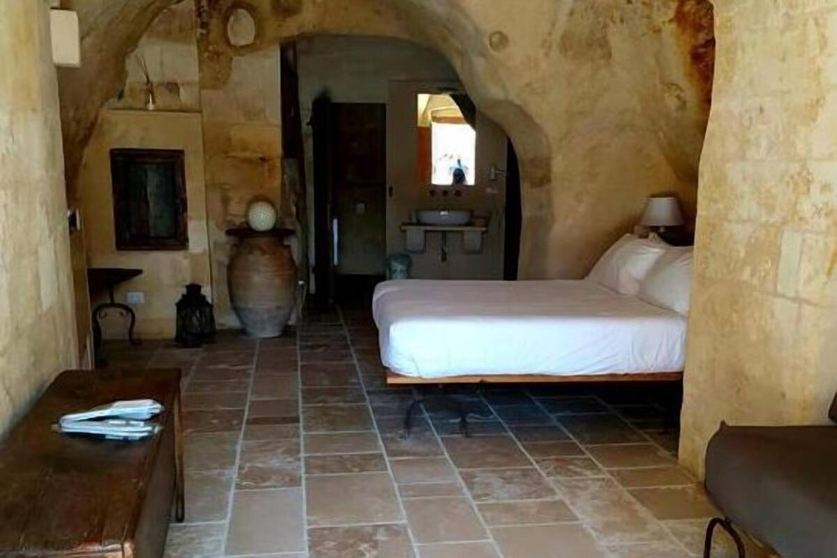 A cozy room with a stone archway, a bed, a wooden bench, and a tiled floor.