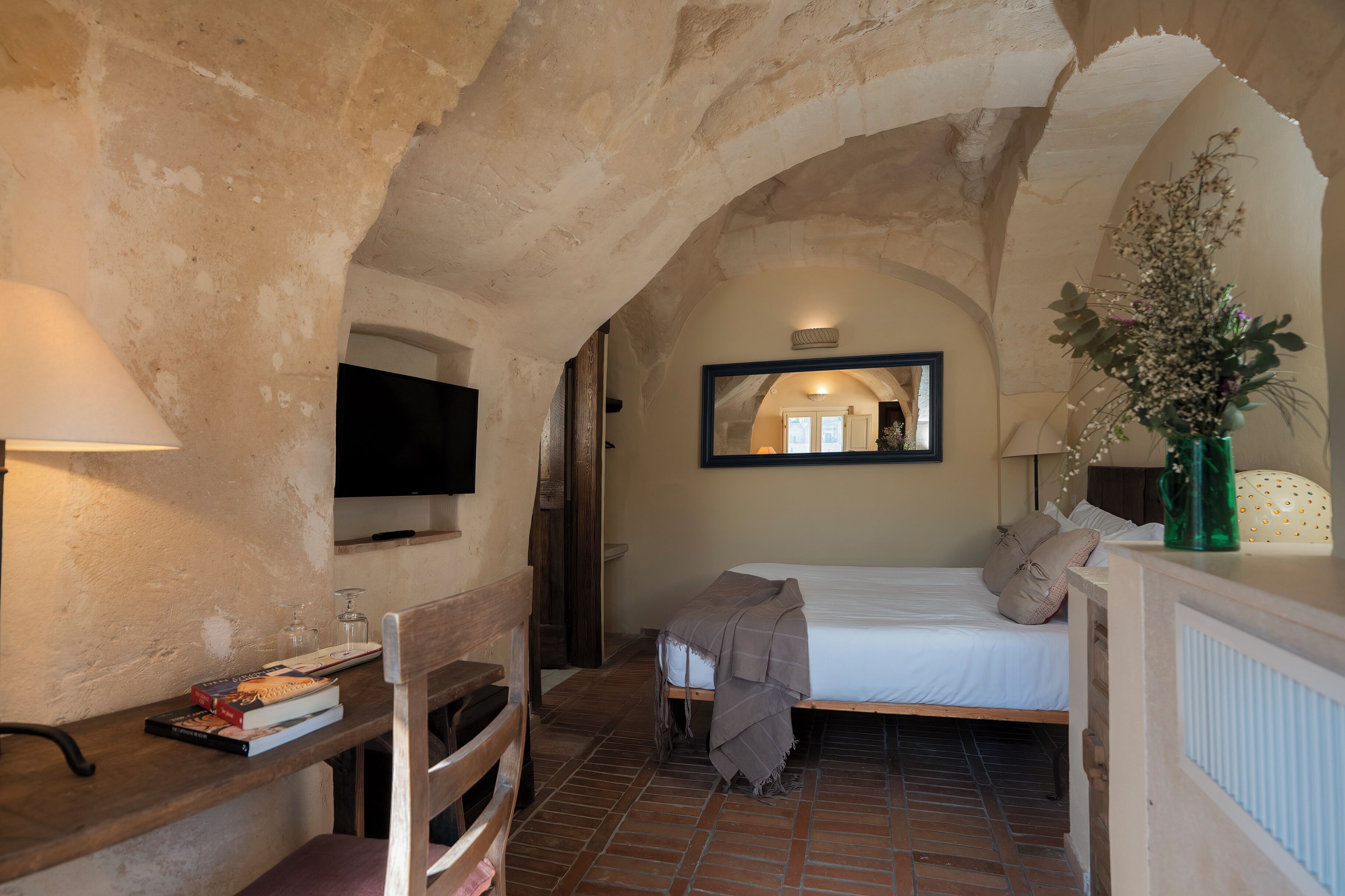 A cozy room with a bed, a TV, a desk with books, and a mirror.