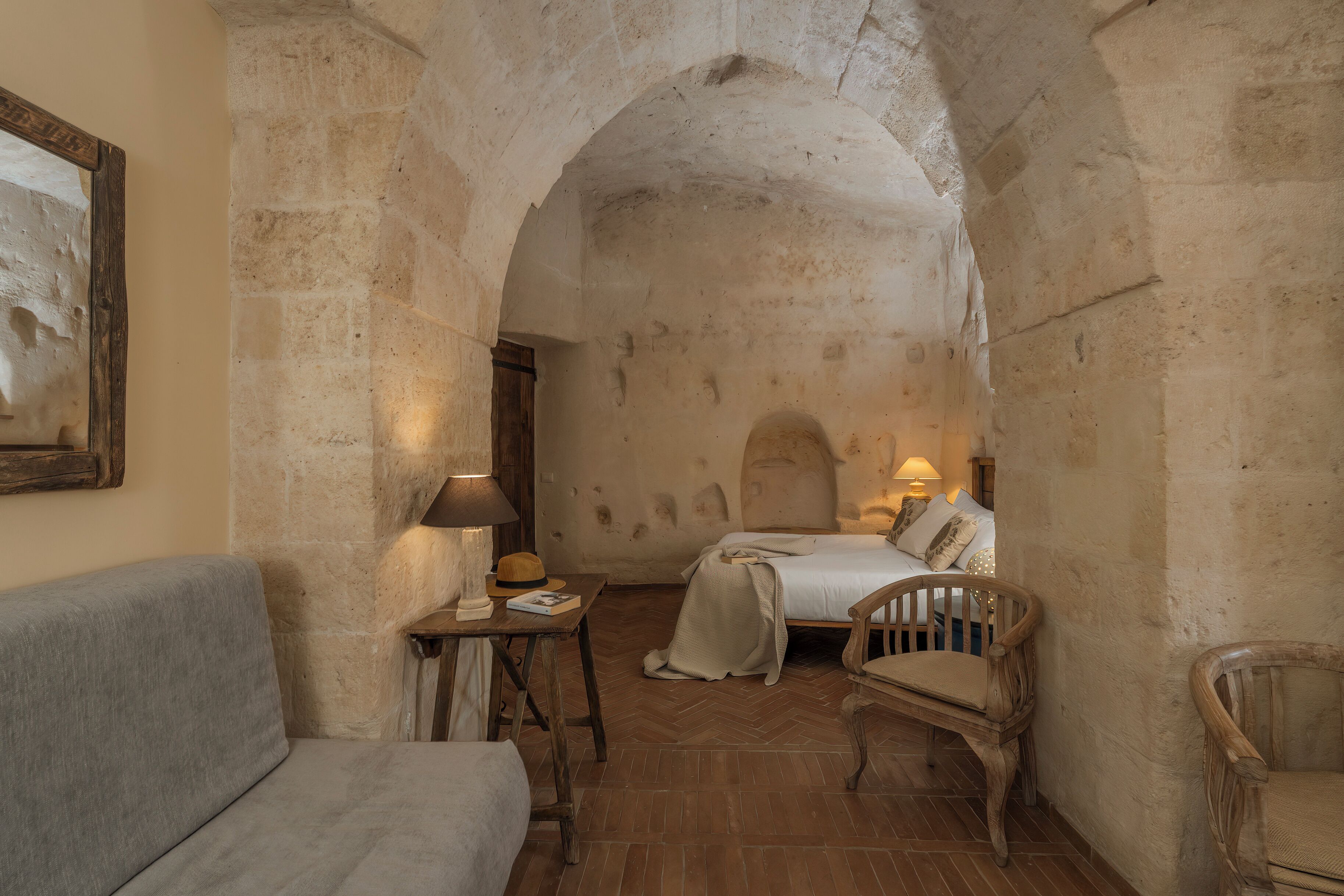 Une pièce rustique comprenant un lit, une chaise en bois, une petite table avec une lampe et un tableau accroché au mur.