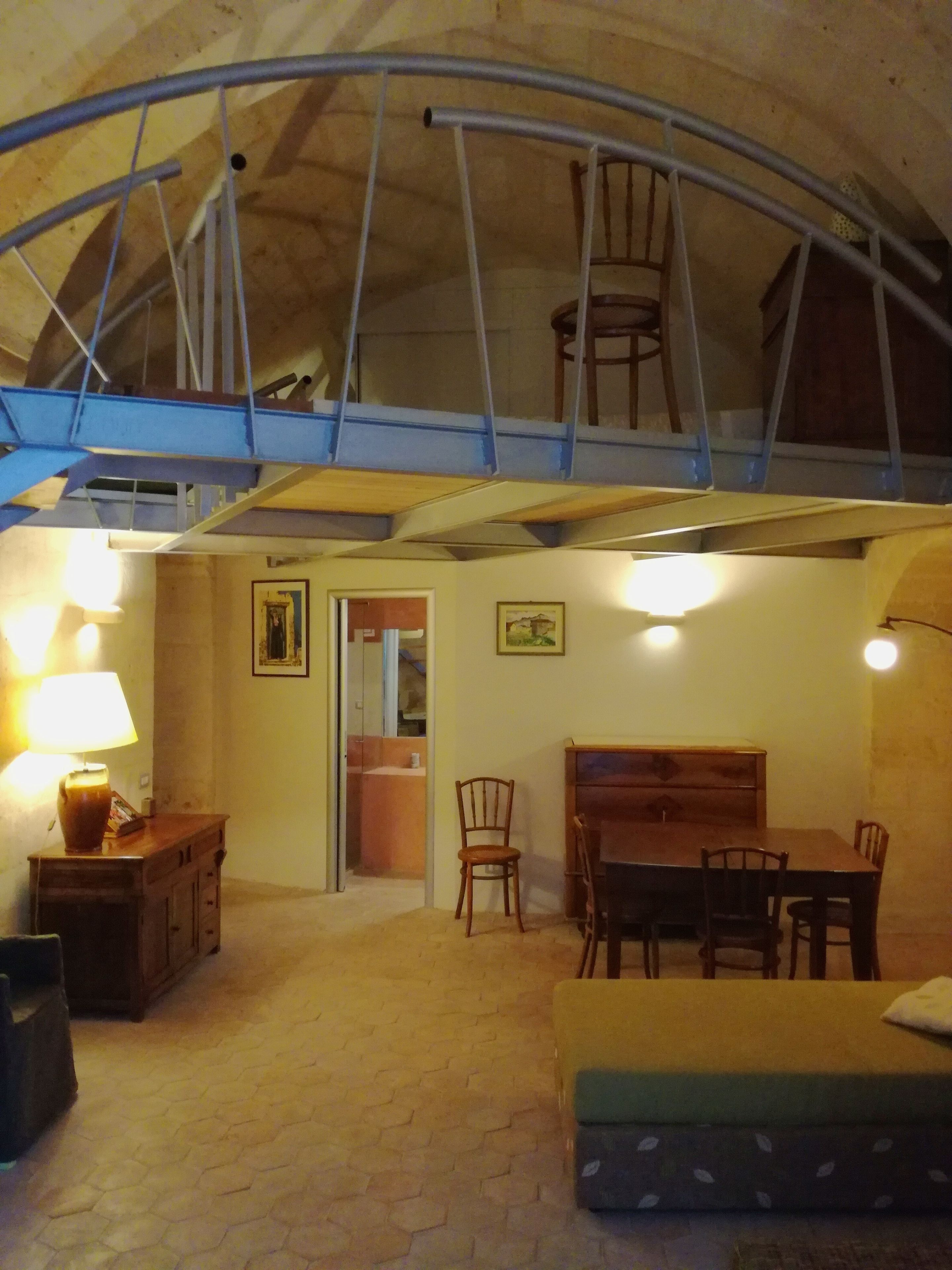 A cozy room with a wooden dining table, chairs, a sofa, and a lamp. There is a staircase leading to an upper level.