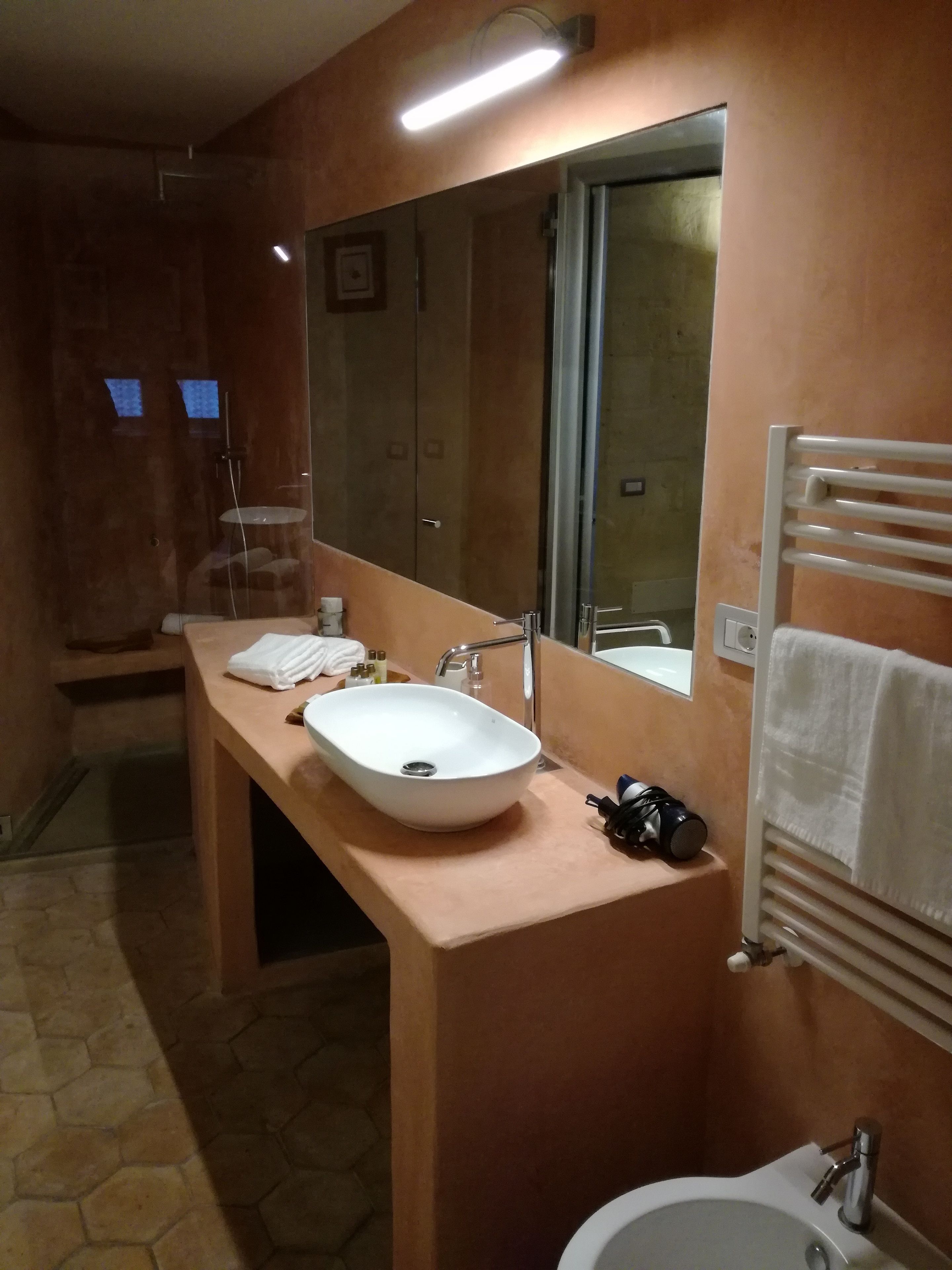 Un baño con un espejo grande, dos lavamanos, un perchero para toallas y una zona de ducha.