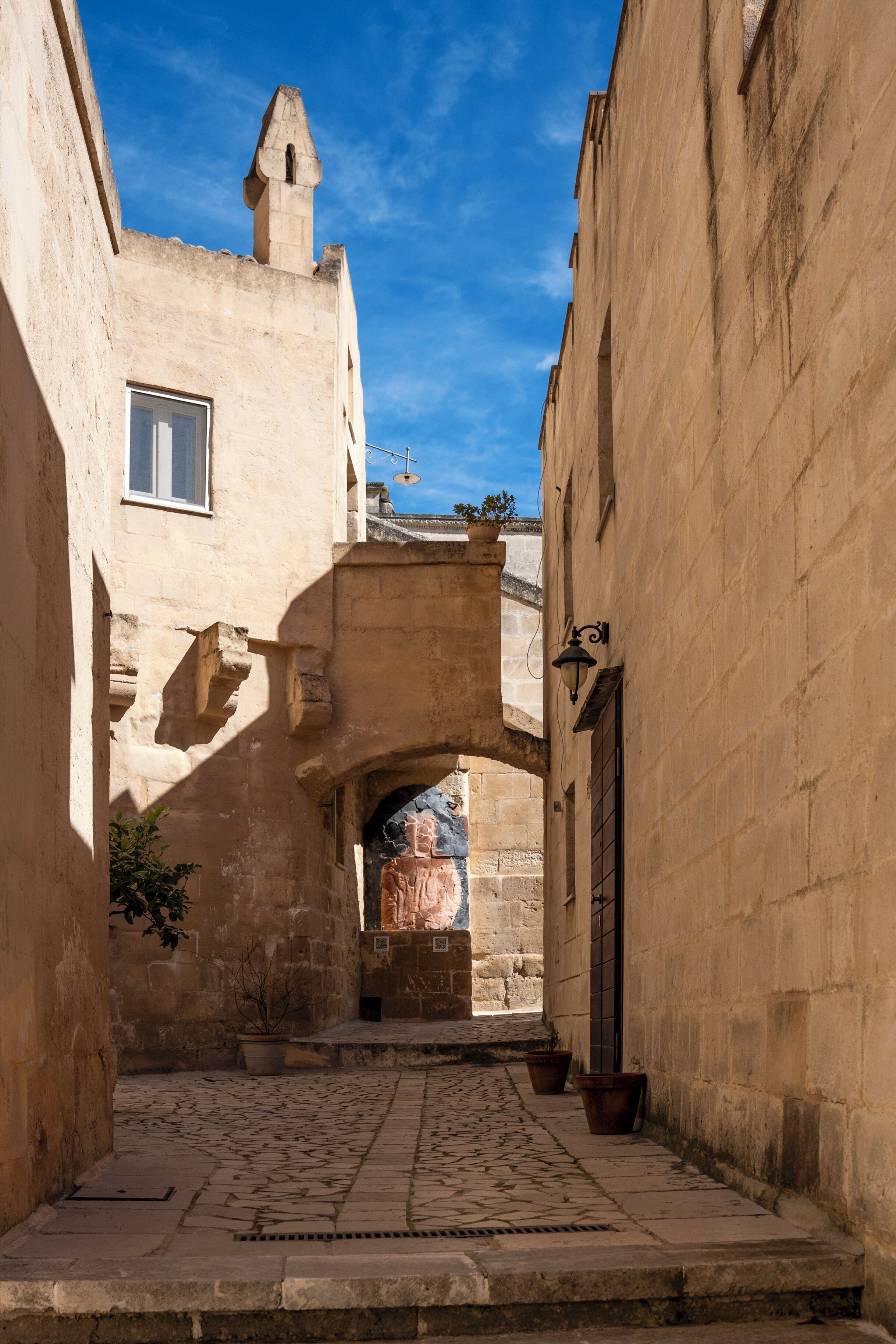 A narrow alleyway with cobblestone pavement, stone buildings, and a small archway.