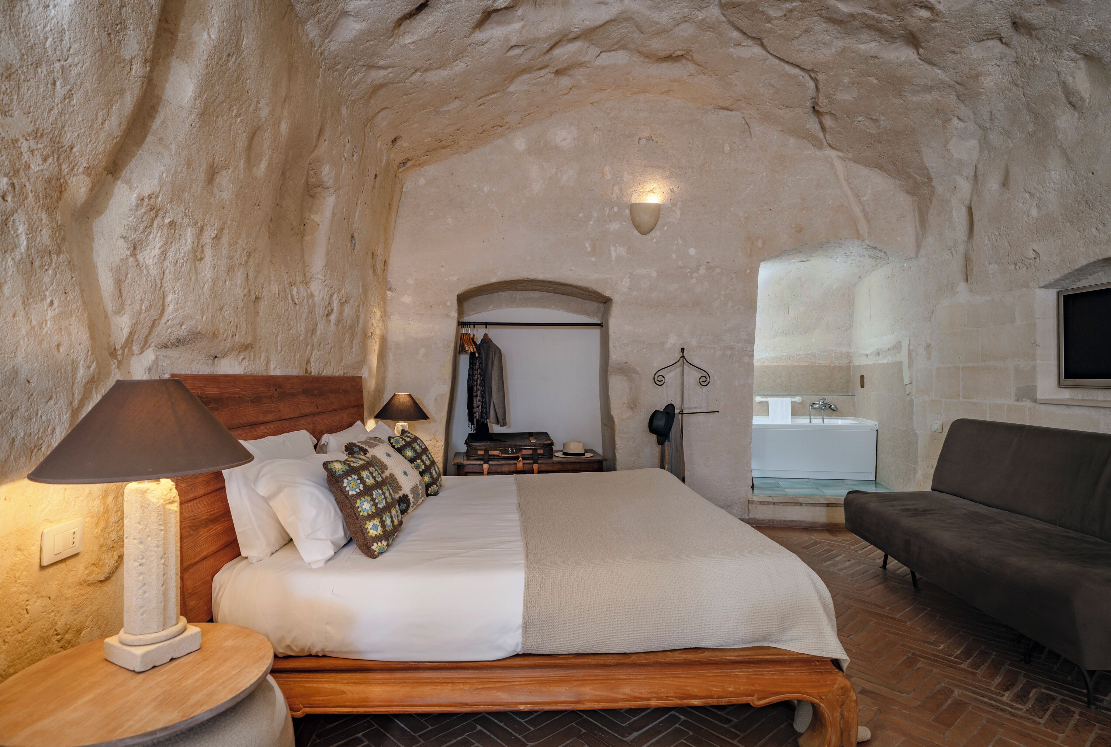 A bedroom with a wooden bed, a round nightstand, a lamp, a wardrobe, and a sofa.
