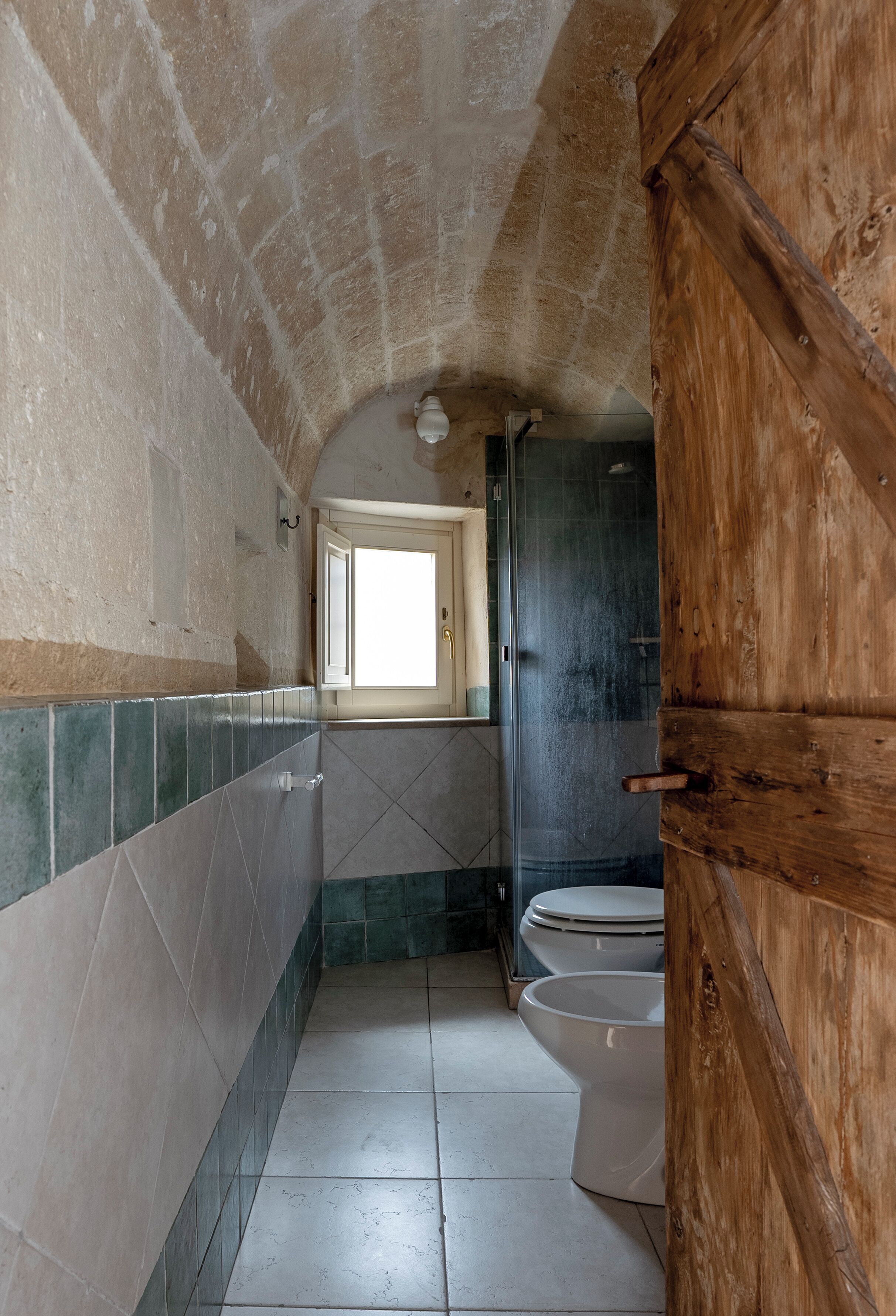 Une petite salle de bain avec un sol carrelé, une porte en bois et un espace douche.