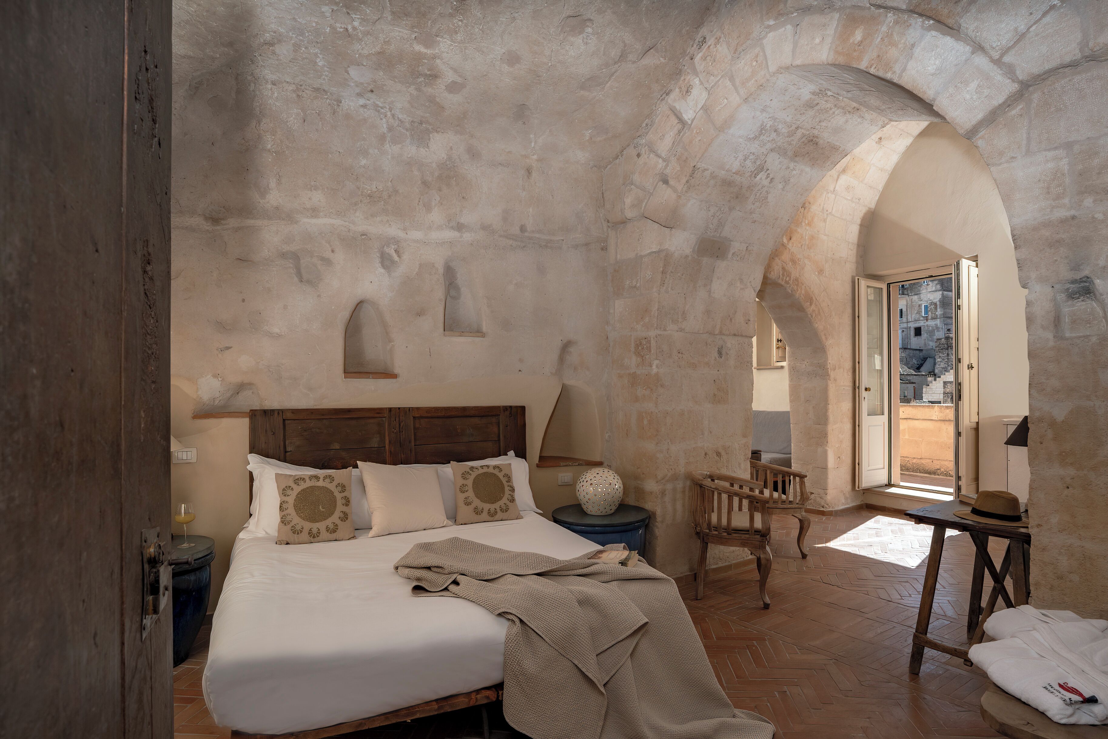 A bedroom with a wooden bed, a nightstand, a chair, and an arched stone ceiling.